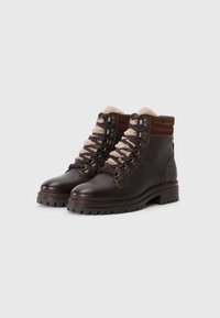 Bruine leren wandelschoenen met een gewatteerde kraag, platte veters, metalen oogjes en een gestructureerde rubberen zool. Voorzien van een zachte, lichtgekleurde voering.