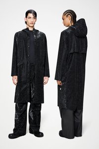 Μαύρο αδιάβροχο με γυαλιστερό, υφασμάτινο μοτίβο, που διαθέτει κουκούλα και κουμπιά, συνδυασμένο με μαύρο, φαρδύ παντελόνι και στιβαρά παπούτσια.
