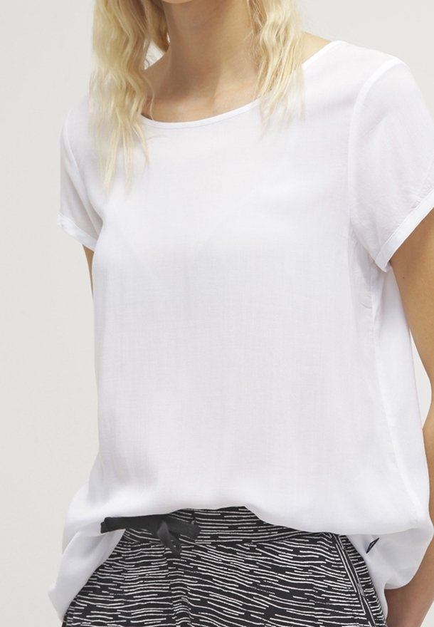 Žena v volné bílé krátkém rukávu blůze zasunuté do kalhot s černobílým vzorem a stahovací šňůrkou v pase.