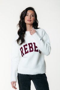Hvit strikket genser med maroon "REBEL" tekst. Designet har rund halsrett og ribbestrikkede mansjetter, parret med mørkegrå bukser.