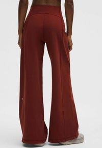 Széles lábú nadrág vörösesbarna anyagból, magas derekú, sima textúrával és oldalsó varrás részletekkel. Aktív használatra alkalmas.