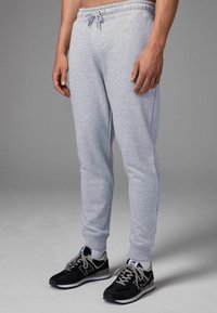 Pantalones de chándal grises hechos de una tela suave, con una cinturilla elástica con cordón, puños acanalados y un corte relajado. Combinados con zapatillas negras.
