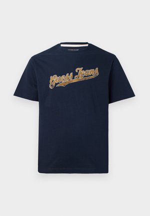Navy blue cotton t-shirt with short sleeves, featuring a textured gold "Guess Jeans" logo across the chest. Crew neckline.