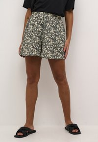 Floral print shorts in dark blue with cream flowers. Elastic waistband, relaxed fit, and smooth fabric. Paired with black slide sandals.