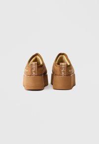 Barna velúr platform cipők lekerekített kialakítással, texturált talppal és hátsó márkajelzéssel. Puha, bélelt belső tér a kényelem érdekében.