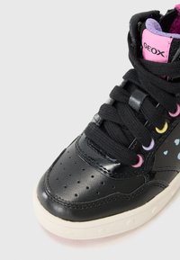 Czarne sneakersy za kostkę z błyszczącą skórzaną cholewką, perforacjami na palcach, kolorowymi oczkami i białą gumową podeszwą.