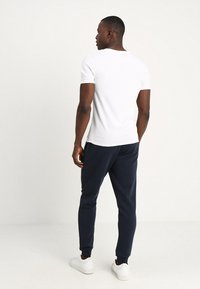 White cotton t-shirt and navy sweatpants, fitted style with ribbed cuffs, paired with white sneakers. Clean design, no visible patterns.
