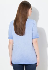 Svetle modré bavlněné tričko s krátkými rukávy, s volným střihem a jemnou gradientní texturou. Zadní strana je hladká s zakulaceným lemem.