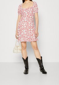 Rotes und weißes Blumendruck-Minikleid mit Puffärmeln, quadratischem Ausschnitt und ausgestelltem Saum. Schwarze Cowboy-Stiefel und eine kleine weiße Handtasche.