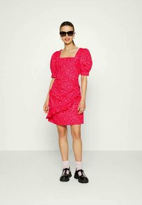 Vestido de padrão floral vermelho com mangas bufantes, decote quadrado e detalhe franzido. Combinado com sapatos chunky pretos e meias rosas.