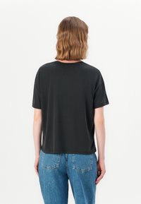 Svart t-skjorte med kort erm og avslappet passform, rund hals og myk stoff. Kombinert med høyhansett blå denimbukser.