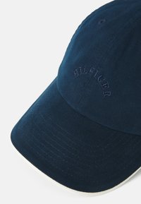 Mørkeblå bomulds-baseballcap med buet skygge, udstyret med broderet "HILFIGER"-logo i matchende tråd, struktureret overflade og hvid underkærm.