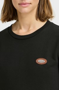 T-shirt nera in cotone con scollatura rotonda, dotata di una piccola etichetta in pelle marrone con il testo "oxmo" nell'area del petto.