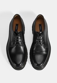 Chaussures en cuir noir avec une finition brillante, dotées d'un bout arrondi, d'un laçage et d'une semelle en caoutchouc texturée. Intérieur avec doublure en tissu léger.