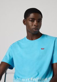 Lichtblauwe katoenen t-shirt met een ronde hals en korte mouwen. Heeft een klein rood Levi's logo op de borst en een tie-dye patroon aan de onderkant.