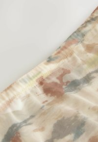 Tessuto trasparente con un motivo astratto multicolore in morbido beige, pesca e azzurro chiaro, caratterizzato da cuciture visibili lungo il bordo.