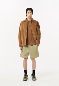 Brun kordflorskjorta över en brun polo, tillsammans med kakifärgade shorts. Svarta strumpor och kamouflage sneakers kompletterar outfiten.