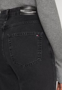 Los vaqueros de mezclilla negros presentan una etiqueta de cuero de Tommy Hilfiger en la parte trasera de la cintura, con un único bolsillo trasero y un sutil detalle del logotipo tricolor.