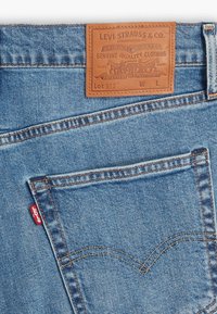 Jean en denim bleu avec patch en cuir Levi's et étiquette rouge Levi's sur la couture de la poche arrière.