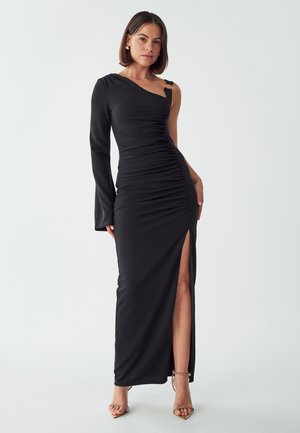 Black one-shoulder dress with ruched texture, featuring a thigh-high slit and a metal accent on the strap. Smooth fabric with fitted silhouette.