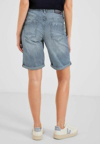 Blårandiga jeansshorts med uppvikta fållar, två bakfickor och subtila blekningar, tillsammans med vita sneakers med grå detaljer.