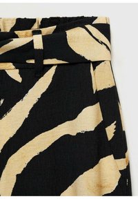Tissu noir et beige avec un motif audacieux de rayures zèbre ; taille élastique avec un devant plat, offrant un aspect texturé.