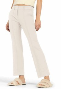 Beige flared trousers with front seams, flat front waistband, and clean-cut hem. Paired with fuzzy slide sandals in a light tan color.