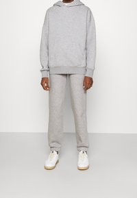 Hoodie et pantalon de survêtement gris en tissu doux et brossé. Le hoodie comprend une poche kangourou et des poignets côtelés ; le pantalon a des chevilles élastiques, porté avec des baskets blanches.