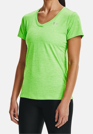 Femme portant un t-shirt de sport vert vif à manches courtes et col en V avec un petit logo sur la poitrine et un pantalon noir.