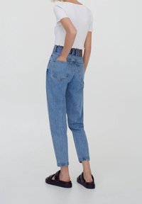 Des jeans taille haute bleu clair présentent une jambe fuselée, des poches arrière et une légère décoloration. Associés à un top court blanc et des sandales noires.