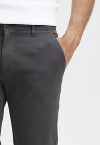 Gray cotton trousers with a slim fit, featuring a side pocket and a brown button detail on the waistband, smooth texture and clean lines.