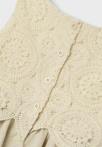 Spitzenoberteil in Creme mit kunstvollen, kreisförmigen Häkelmustern und vier Knöpfen. Leicht, mit einer sanften Textur und elegantem Design.