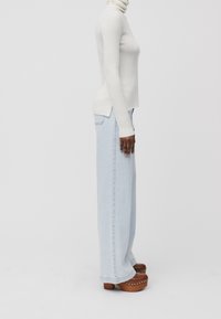 Pull col roulé blanc côtelé associé à un jean large bleu clair et des sabots compensés marron. Matériaux à fort contraste et coupe décontractée.