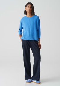 Lichtblauw geribbeld sweater met een ronde hals, gecombineerd met marineblauwe wijde broek en blauwe sneakers met witte strepen.