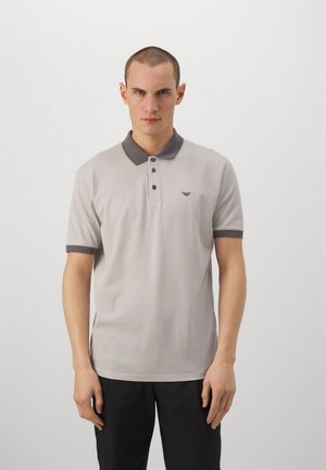 Polo de color gris claro con un collar gris oscuro, tapeta de tres botones y un pequeño logo en el pecho. Tejido suave, mangas cortas.