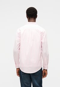 Ροζ ανοιχτό και λευκό ριγέ πουκάμισο με μακριά μανίκια, μανσέτες με κουμπιά, καμπυλωτό τελείωμα και σχεδιασμό στο πίσω μέρος. Φοράται με σκούρο τζιν παντελόνι.