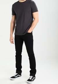 Šedé tričko s krátkým rukávem, černé úzké džíny a černé tenisky s bílými tkaničkami. Jednoduchý design s minimálním zdobením.