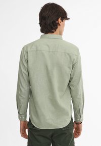 Camisa de manga larga, de color verde claro, hecha de tejido texturizado, con cuello tipo button-down, puños abotonados y dobladillo curvo.