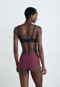 Black bralette with sheer panels and adjustable straps, paired with high-waisted maroon briefs. Smooth texture, minimalistic design.
