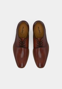 Chaussures habillées en cuir marron avec une finition brillante, présentant un bout pointu et un design à lacets. L'intérieur est doublé en cuir beige.