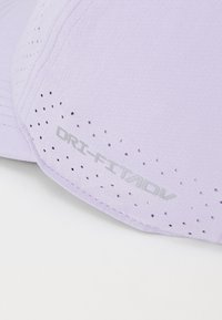 Lys lilla caps med en glatt tekstur, som har perforeringer for ventilasjon og sølvfarget "DRI-FIT/ADV" logo på siden.