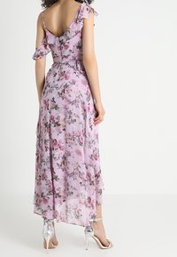 Lång blommig klänning i ljuslila tyg med volangärmar, med en V-rygg och en hög-låg nederkant. Bärs med silverfärgade högklackade sandaler.