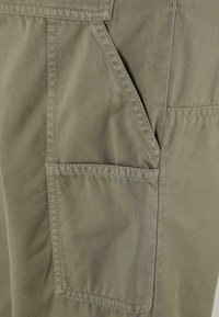 Khaki cargo-housut, joissa on useita taskuja, sileä pinta, kestävä kangas ja näkyvät ompeluyksityiskohdat lisäävät voimaa.