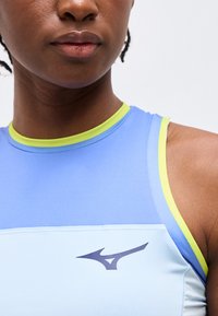 Κοντινό πλάνο ενός ατόμου που φοράει μπλε και ανοιχτό μπλε αμάνικη αθλητική μπλούζα με πράσινο περίγραμμα και μαύρο λογότυπο Mizuno στο στήθος.