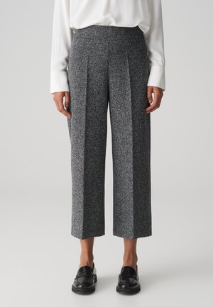Pantaloni tweed a gamba larga in bianco e nero con un motivo testurizzato, caratterizzati da una vita alta e pieghe frontali. Abbinati a mocassini neri.