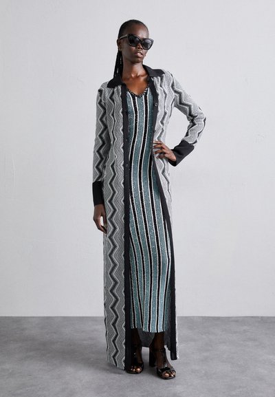 Ilgas, su mygtukais užsegamas paltas juodai baltu zigzaginiu raštu, uždėtas ant dryžuotos mėlynai juodos suknelės. Juodi saulės akiniai ir atviri bateliai.