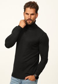 Black turtleneck sweater made of knit fabric with a fitted design, ribbed cuffs, and waistband. Worn with denim jeans.
