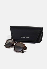 Ochelari de soare cu model tortoiseshell maro, cu lentile închise, alături de un toc de piele neagră, ce poartă branding-ul argintiu "MICHAEL KORS".