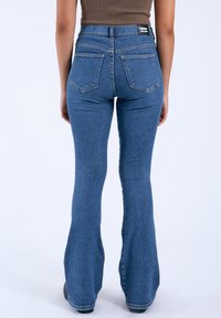 Vaqueros de pierna acampanada de cintura alta en denim azul claro, con una cintura ajustada, costuras mínimas y dos bolsillos traseros con una etiqueta en la cinturilla.