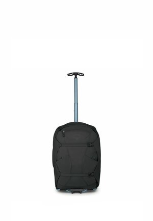 Bolsa de lona negra con ruedas, asa telescópica extendida y correas de compresión en la parte delantera, de pie sobre fondo blanco.